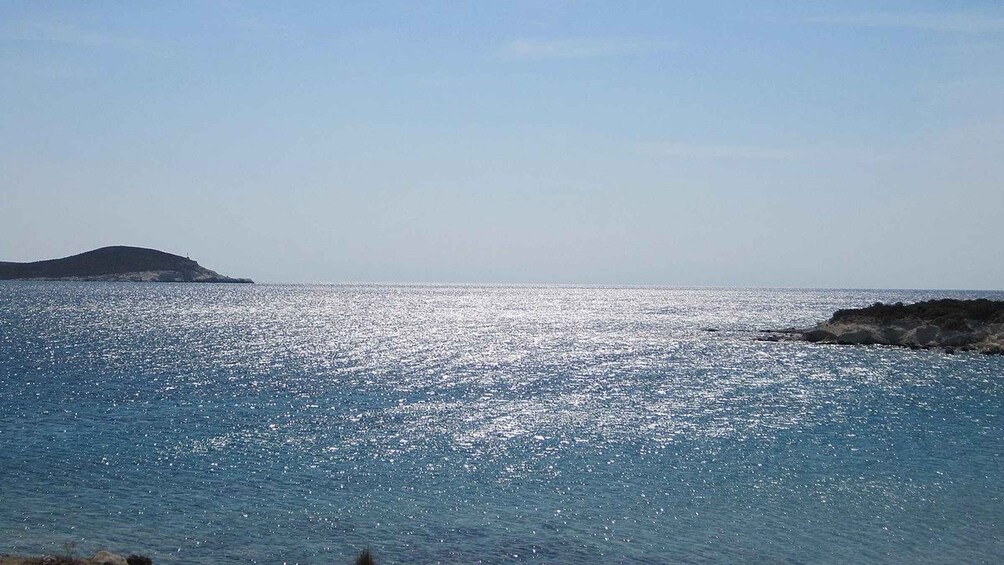 A calm sea with a rocky outcrop on the right and a distant island. 1