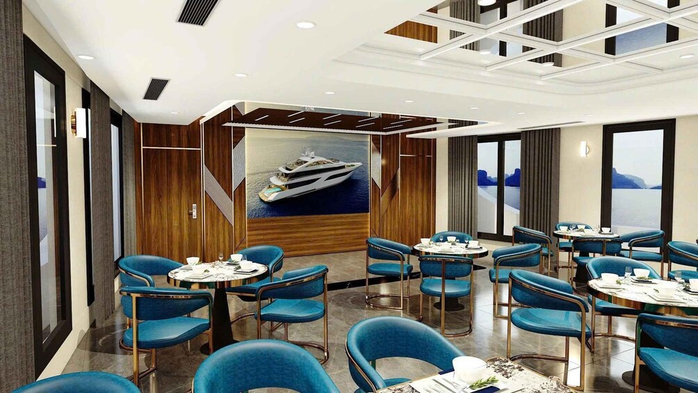 A modern dining area with blue chairs and round tables, a large painting of a yacht, and a view of the sea through large windows. 2