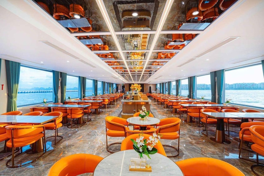 A cruise ship dining area with orange chairs and tables, large windows overlooking the sea, and a modern ceiling design. 4