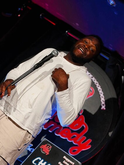 A person holding a microphone on a stage with a backdrop that includes the text 'Comedy Club' and 'Support Live Comedy.' 5