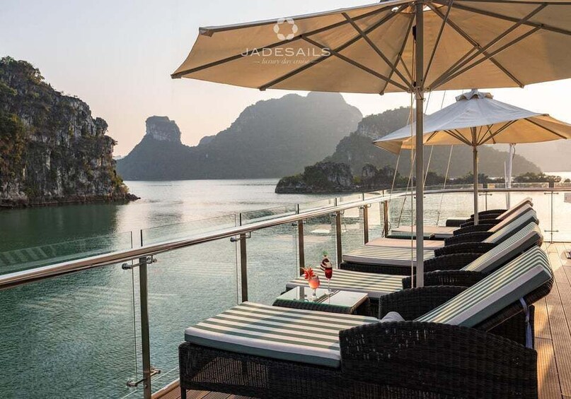 A deck with lounge chairs and umbrellas overlooking a body of water with cliffs in the background. 4