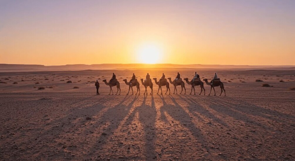A group of people riding camels in a desert at sunset. 3
