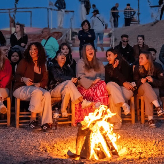 A group of people sitting around a campfire at dusk. 2