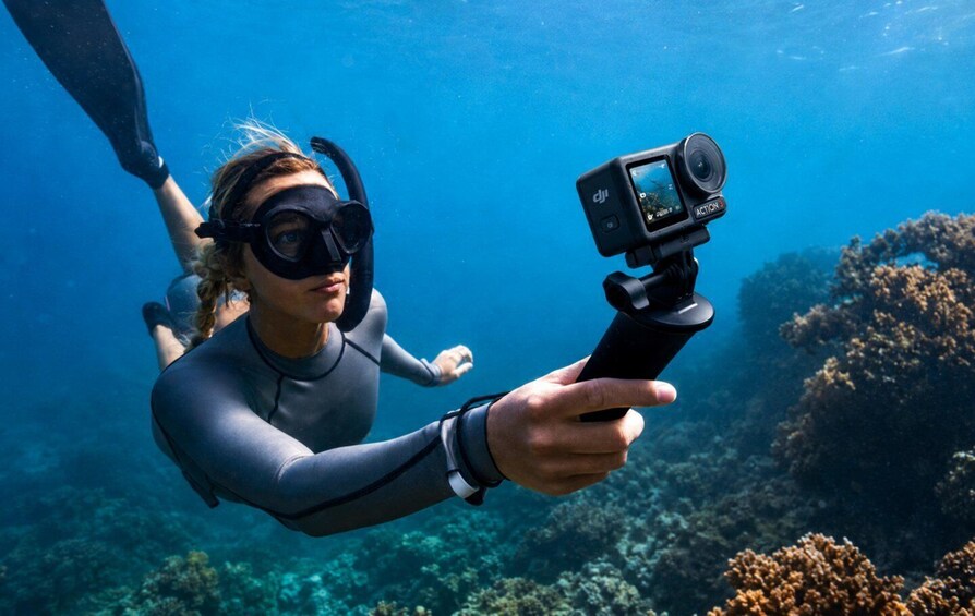 A person scuba diving underwater, holding a camera on a tripod. 4