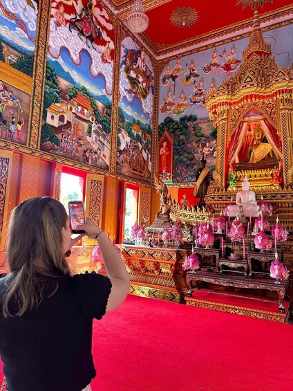 A person taking a photo inside a temple with intricate murals and a golden statue. 2