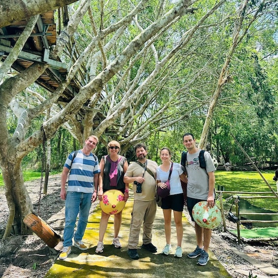A group of people standing under a tree with a wooden structure overhead. 4