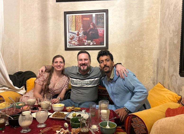 Three people seated on a couch with a table full of food and drinks in front of them. 1