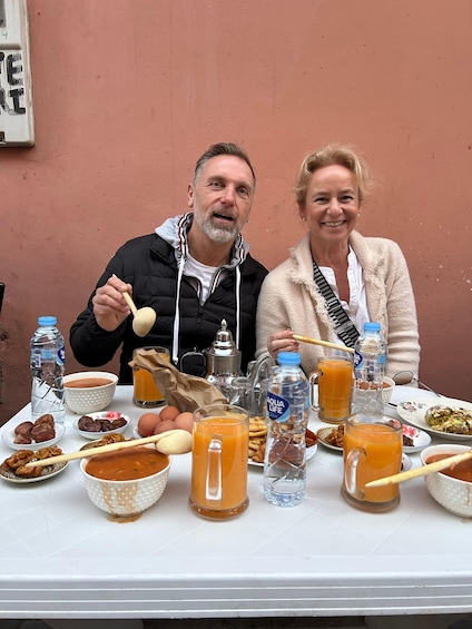 Two people sitting at a table with various food items and drinks. 4