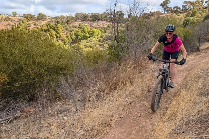 A person riding a mountain bike on a dirt trail surrounded by dry vegetation and trees. 3