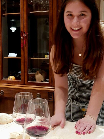 A person leaning over a table with three wine glasses filled with red wine, a wooden cabinet with glass doors, and a small yellow object with a face on the cabinet's shelf. 5