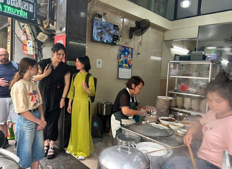 A busy kitchen with chefs preparing food, a television screen, and a neon sign. 3