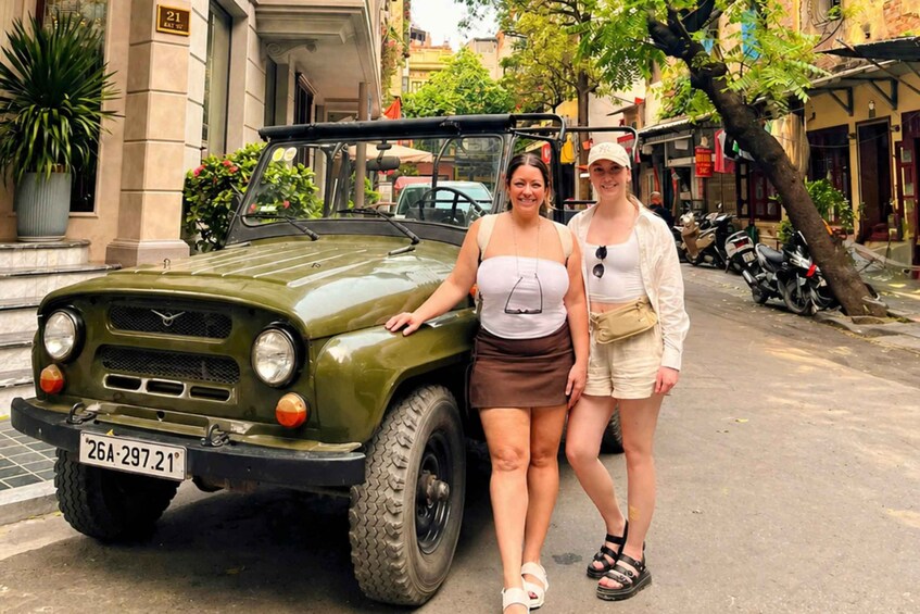 Two people standing next to a vintage military jeep on a city street. 1