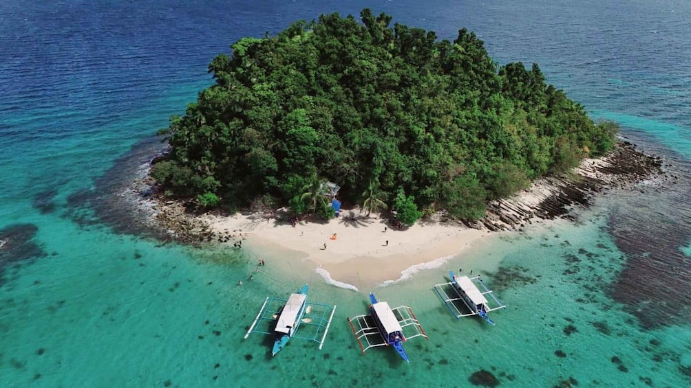 A tropical island with clear turquoise waters, a sandy beach, and several boats anchored near the shore. 4