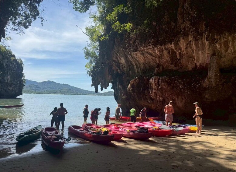 A group of people near a body of water with kayaks and a rocky cliff. 3