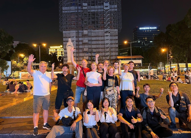 A group of people posing in front of a construction site with a statue and a building labeled 'DIAMOND PLAZA' in the background. 4