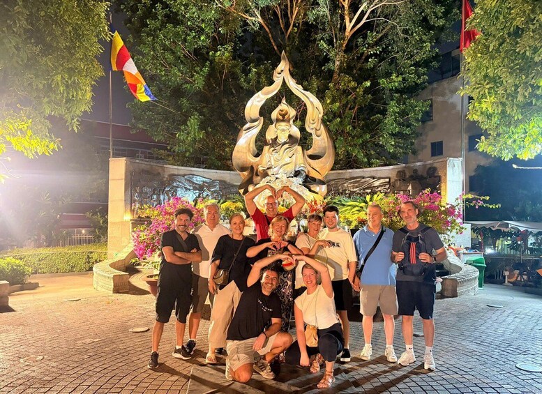 A group of people posing in front of a large sculpture with a flag in the background. 5
