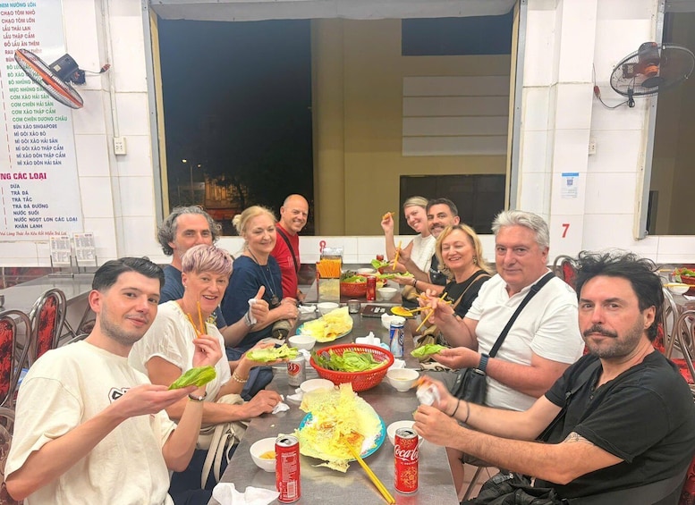 A group of people dining at an outdoor restaurant with a menu on the wall and a fan on the ceiling. 2