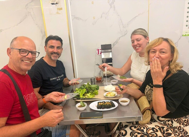 Four people dining at a restaurant with a marble wall and a menu board in the background. 5