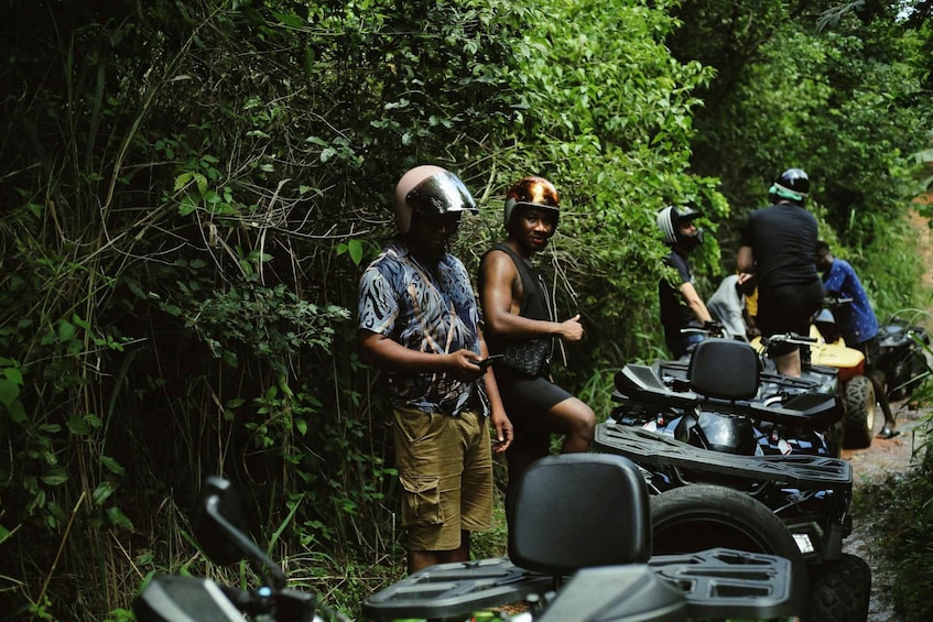 People standing near ATVs in a forested area. 1
