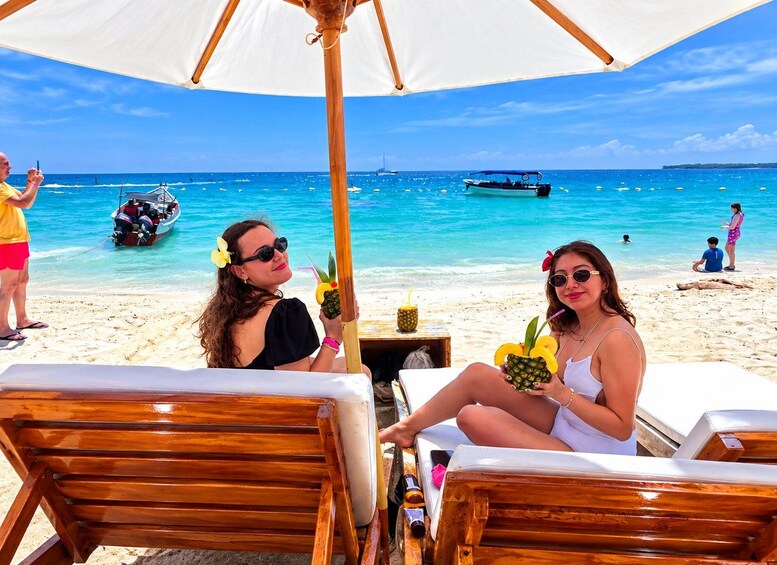 Two people sitting under a beach umbrella on a sandy beach with the ocean in the background. 5