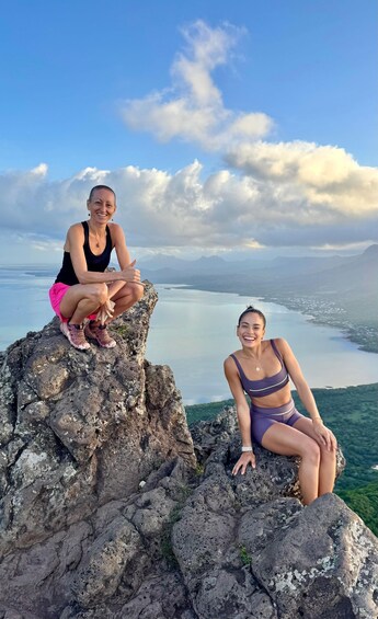 Two people sitting on a rocky outcrop with a lake and mountains in the background. 5
