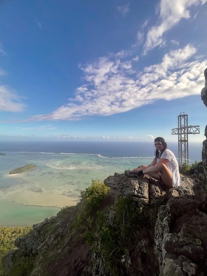 A person sitting on a rock overlooking a coastal landscape with a power line tower in the distance. 5