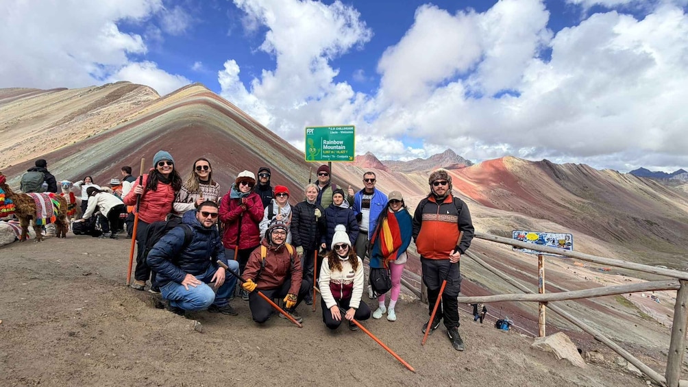 A group of people posing with llamas on a mountain trail, with a sign indicating the Rainbow Mountain and its elevation. 4