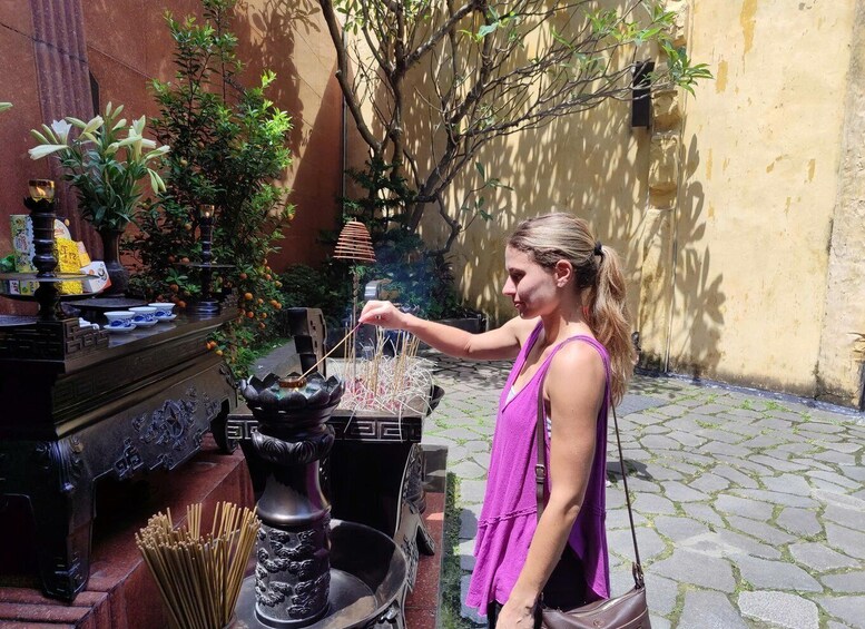 A person performing a ritual with incense sticks in a courtyard with plants and traditional decorations. 4
