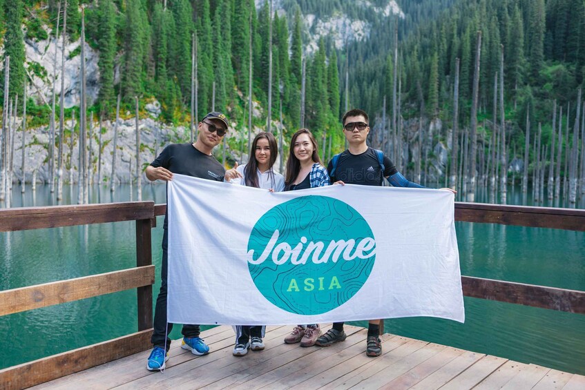 Four people holding a banner with 'Joinme Asia' on a wooden dock by a lake surrounded by trees. 1