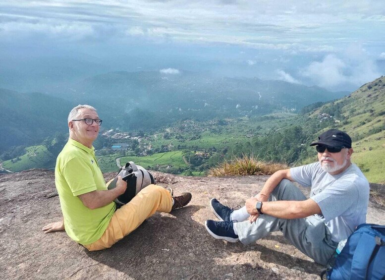 Two people sitting on a rocky outcrop overlooking a valley with green fields and distant mountains. 3