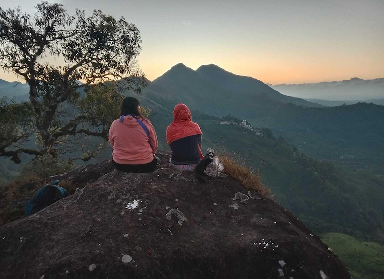 Two people sitting on a rock overlooking a mountainous landscape during sunset. 1