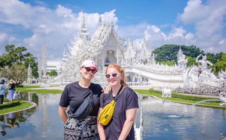 Two people standing in front of a white ornate temple with a pond in the foreground. 1