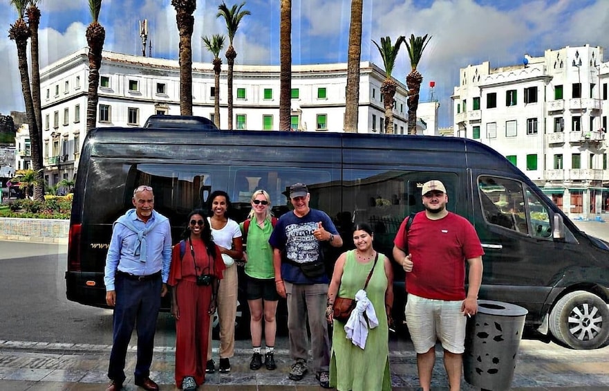 A group of people standing in front of a black van with palm trees and buildings in the background. 2