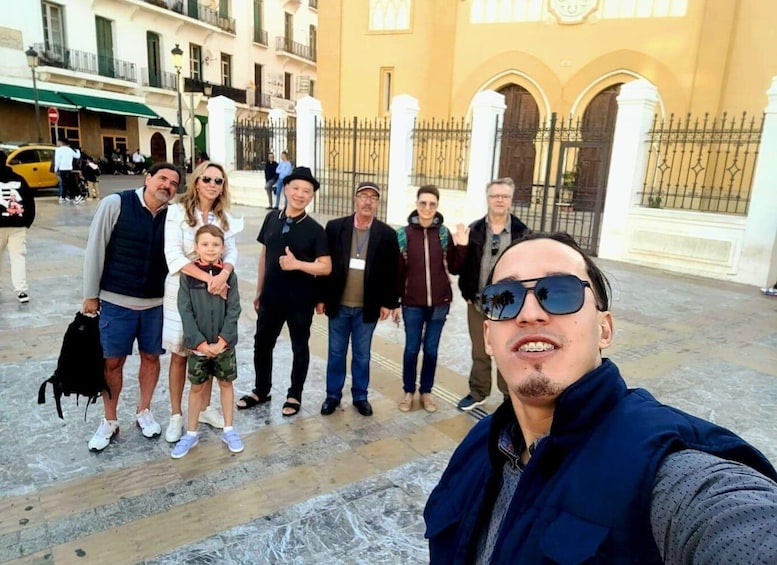 A group of people standing in a courtyard with a yellow building and a wrought iron gate in the background. 4