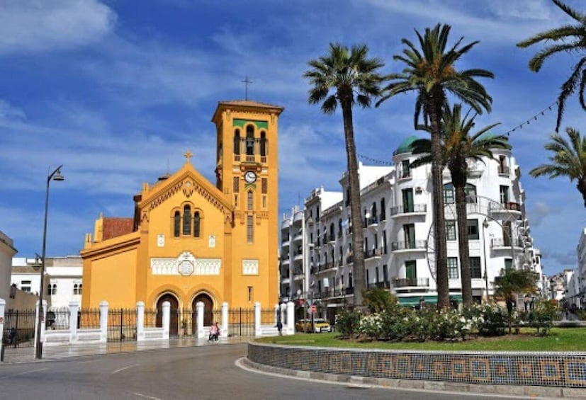 A yellow church with a clock tower, palm trees, and modern buildings. 1