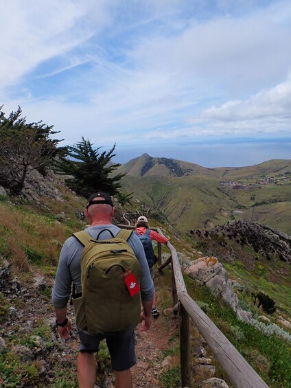 A hiker with a backpack walking on a rocky trail with a view of a valley and mountains in the background. 4