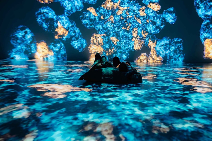 Une personne allongée sur une plateforme flottante, au milieu d’une étendue d’eau, avec des projections de lumière bleue et orange en arrière-plan. 2