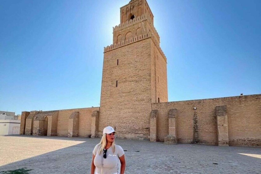 A person standing in front of a historic tower with a clear sky. 1
