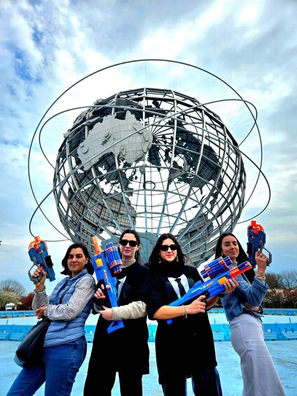Four people holding water guns in front of a large metallic globe structure. 4