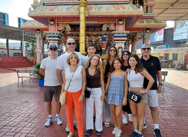 A group of people posing in front of a colorful, ornate structure with intricate designs and a golden pole. 1