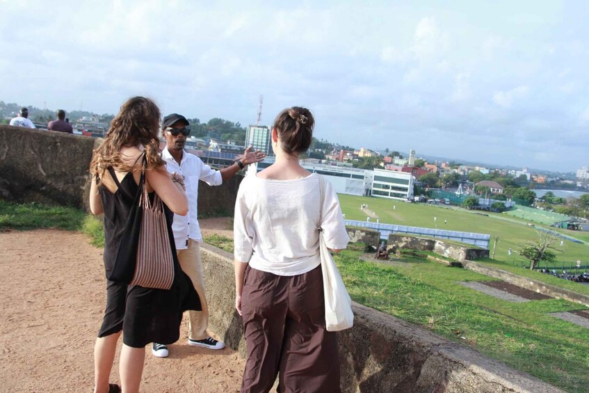 A group of people standing on a stone wall overlooking a grassy field with a bridge in the distance. 3