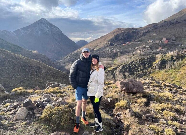 A couple standing on a rocky mountain peak with a valley and mountains in the background. 2