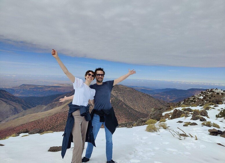 Two people standing on a snowy mountain with arms raised, overlooking a vast landscape of mountains and valleys. 3