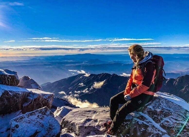 A person sitting on a snow-covered rock with a mountain range in the background. 5