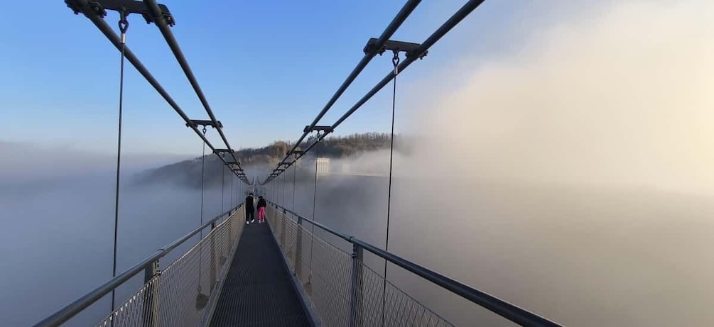 A suspension bridge with metal railings and cables, overlooking a foggy body of water. 3