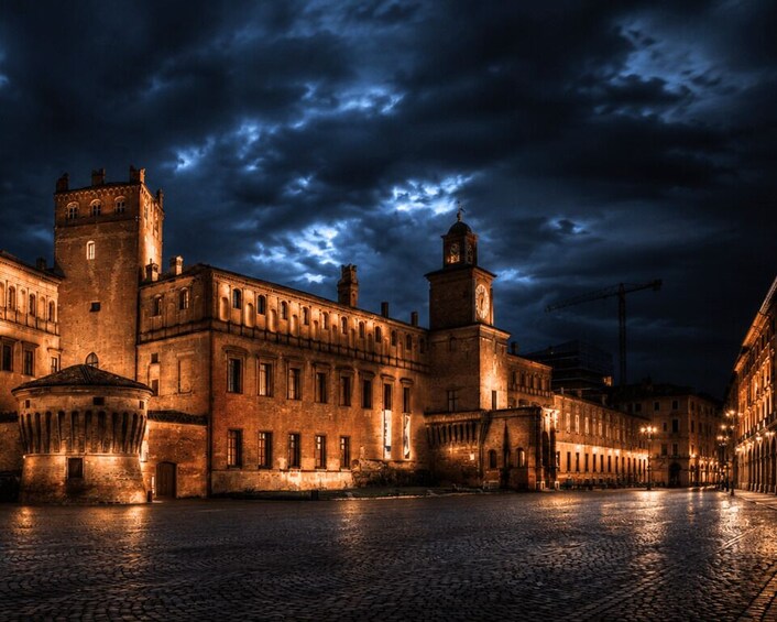 A historic stone building with a tower, a round tower, and a cobblestone street at night. 1