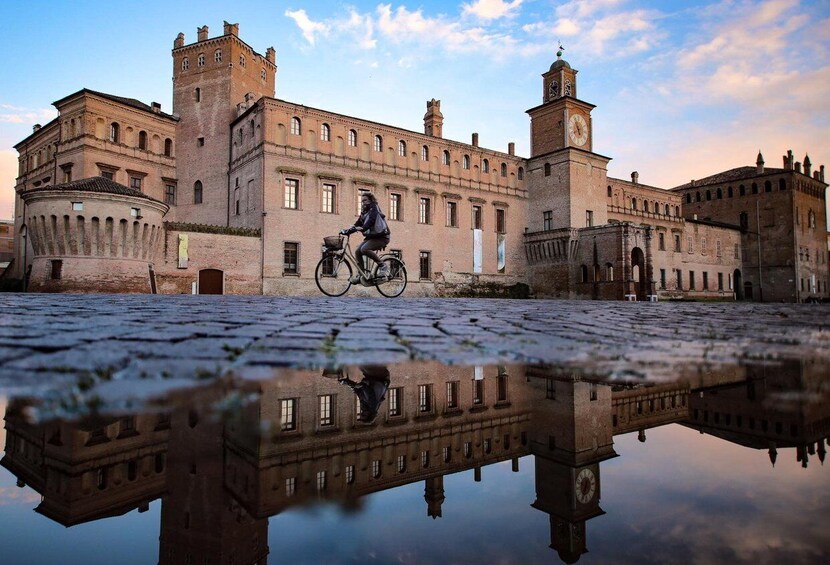 A historic building with a moat, a cyclist, and a clear reflection in the water. 4