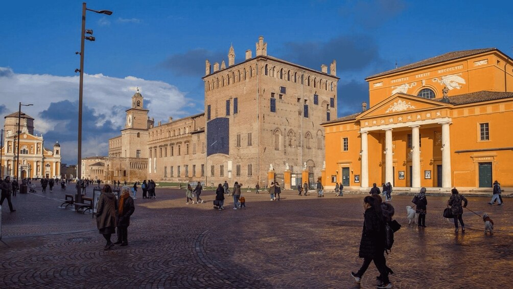 A historic square with cobblestone pavement, a large stone building with a clock tower, and a yellow building with classical columns. 3