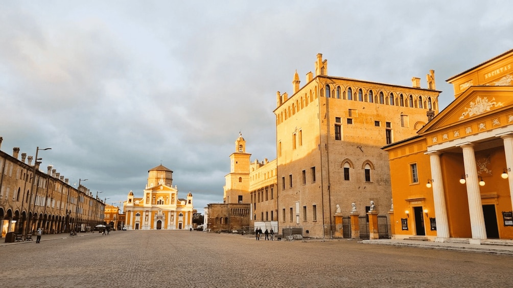 A cobblestone street lined with historic buildings, including a prominent church with a dome and a large, ornate building with columns. 2