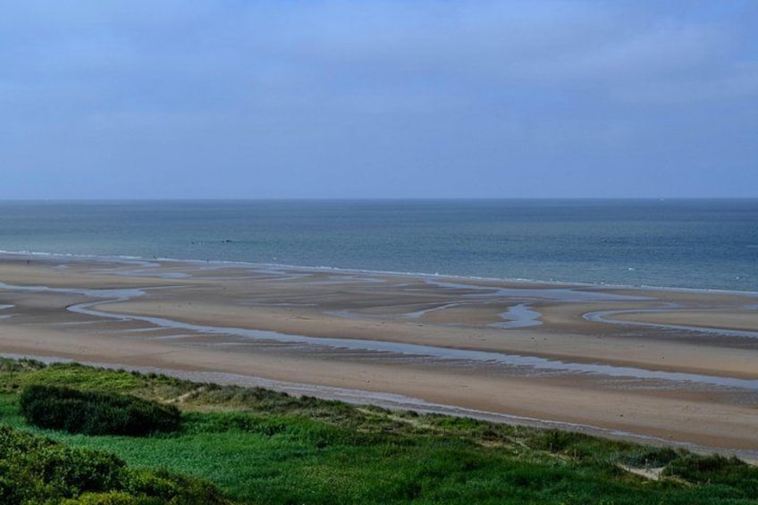 A coastal landscape with a sandy beach, green vegetation, and a calm sea. 3